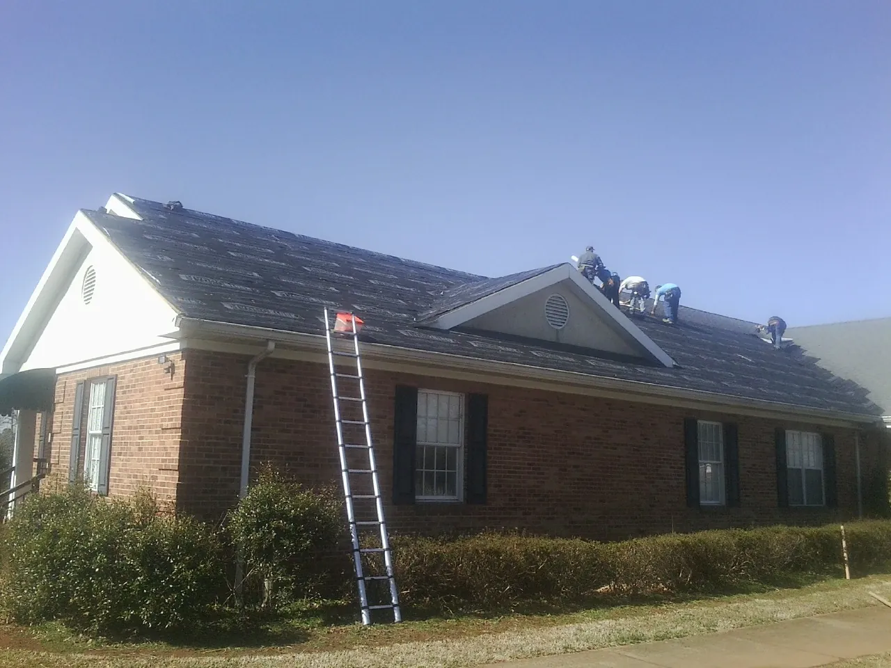 Crew tearing shingles off a brick ranch roof with a ladder set — Emergency Roof Repair work by our crew in Narragansett