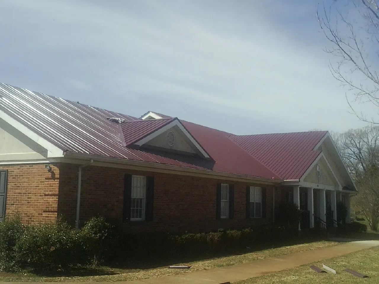 Red metal roof with gabled entries on a long brick building, from a Hail Damage Roof Repair job in Narragansett