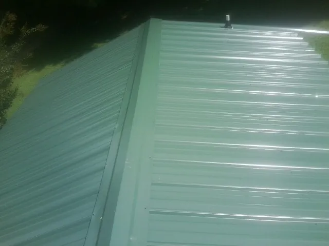 New green metal panels meeting at the ridge of a roof — Flat Roof Repair work by our crew in Narragansett