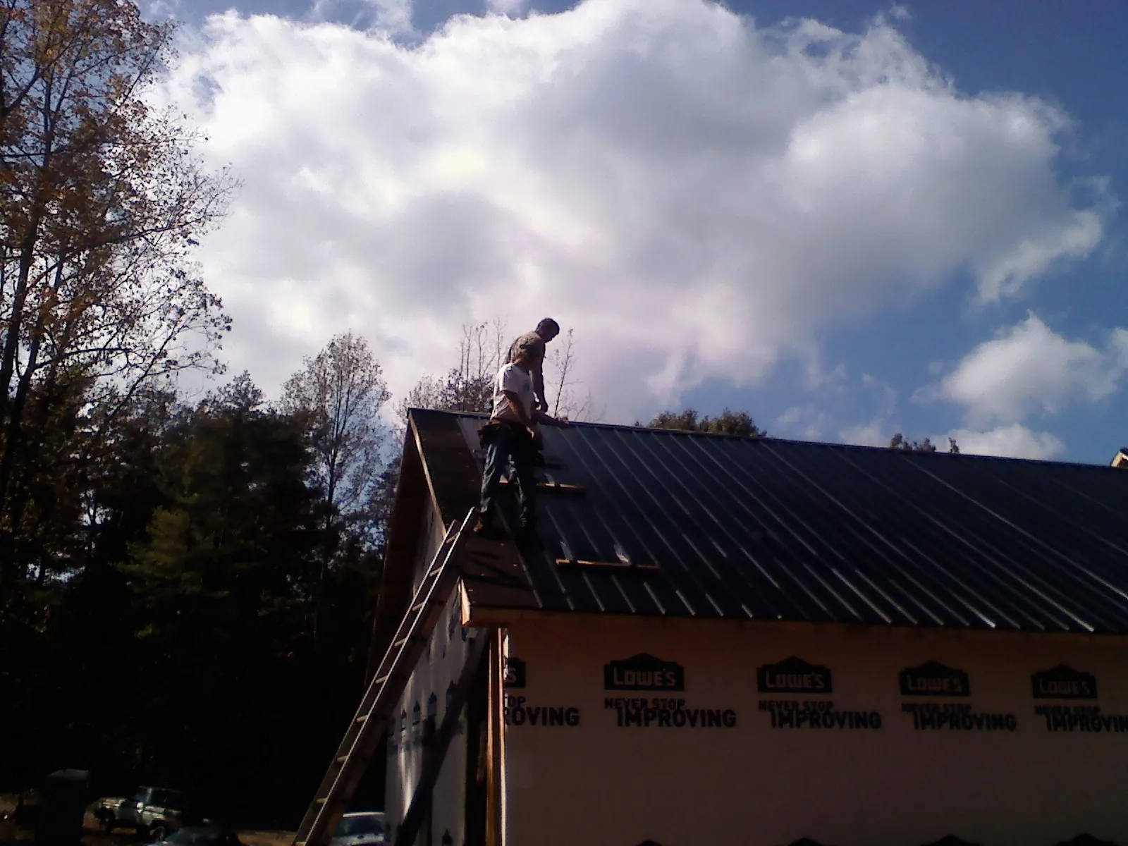 Roofer fastening dark metal panels high against a cloudy sky, from a Roof Inspection job in Narragansett