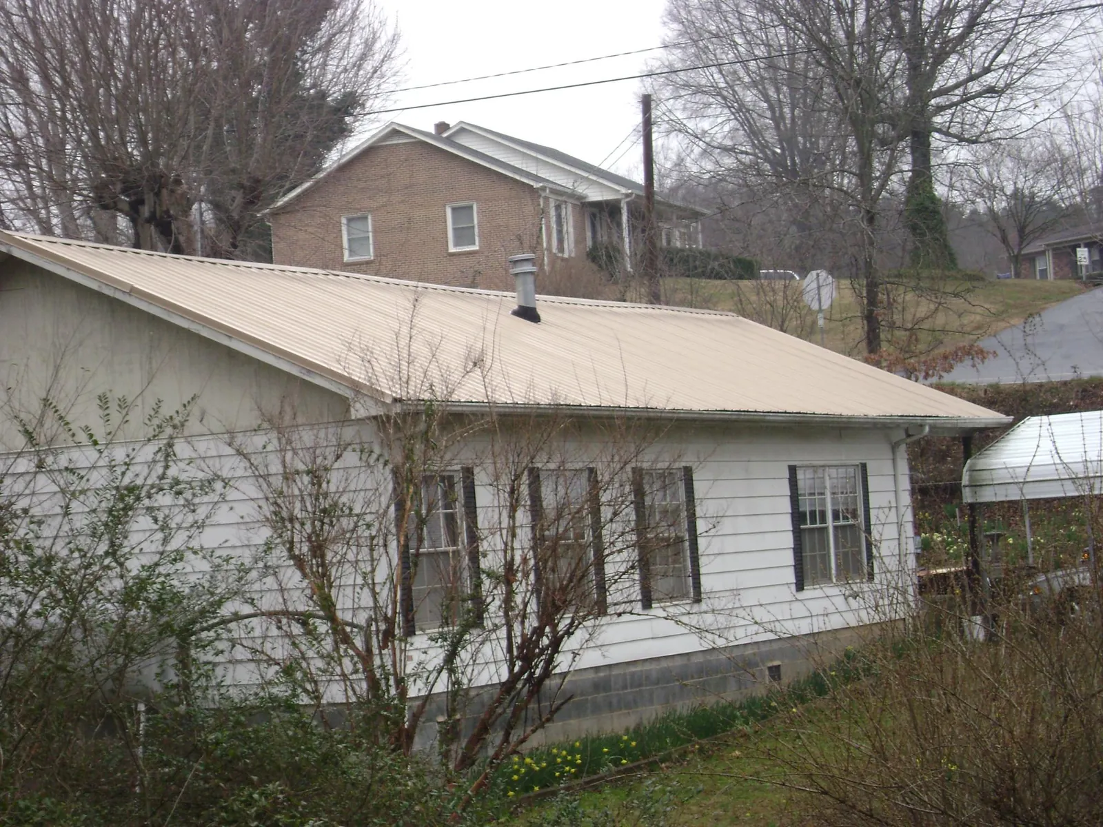 Tan metal roof on a white sided house set into a hillside — Commercial Roofing by Roofing Brothers in Narragansett