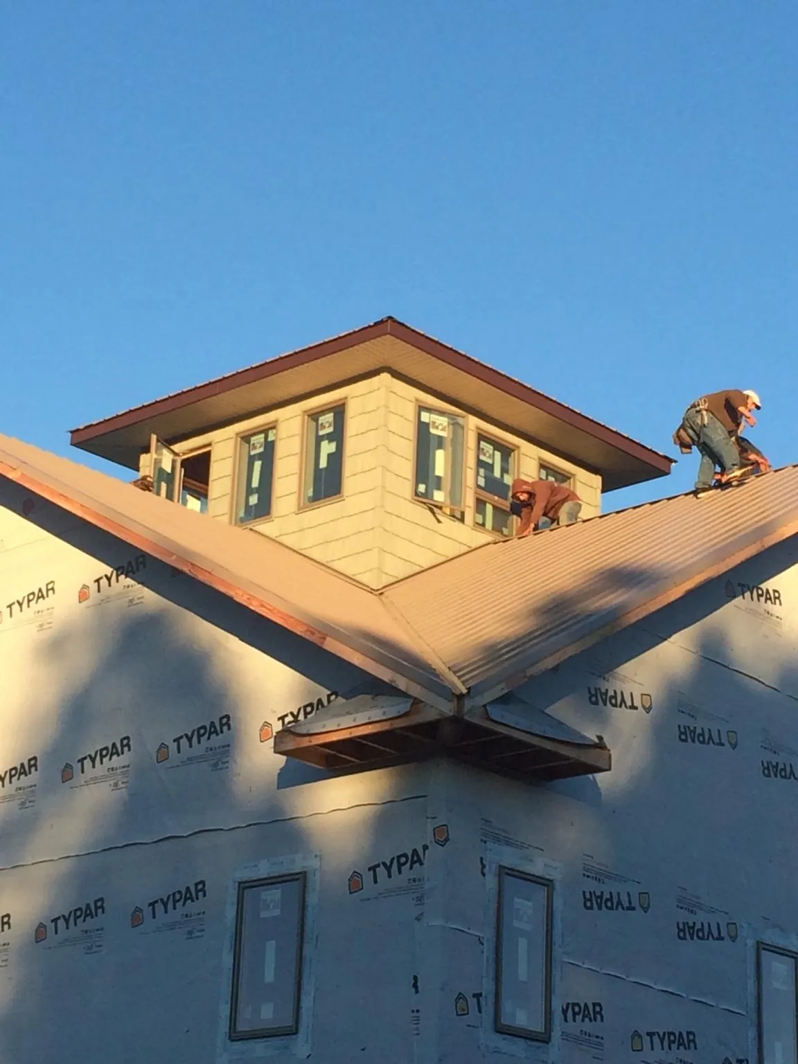 Roofers working around a rooftop cupola on a new metal roof at sunset — Roof Waterproofing in Narragansett by Roofing Brothers